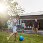 little boy playing soccer outside his home with family