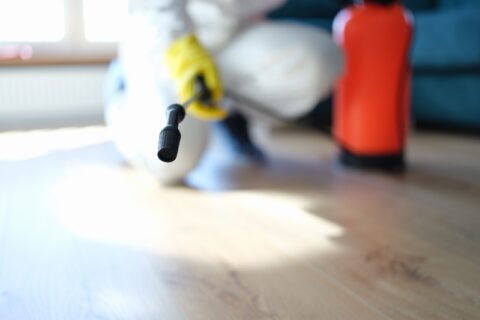 Man in protective suit treating floor in apartment with disinfectant closeup.